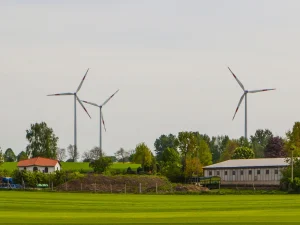 Budovy ve venkovské krajině, v pozadí trojice větrných elektráren.