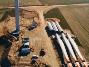 Konstrukce větrné elektrárny v exteriéru, na zemi leží lopatky a další součásti. 